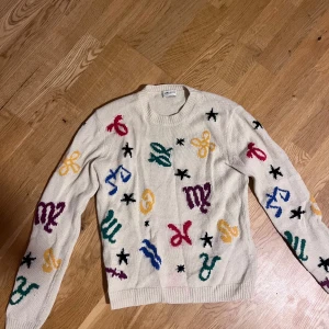 Saint Laurent stickad tröja med mönster - Beige stickad tröja från Saint Laurent med coola färgglada symboler och stjärnor över hela plagget. Tröjan har rund halsringning, ribbade muddar och lång ärm. Perfekt för dig som vill sticka ut med en unik designertröja. Står M men passar mer S och XS