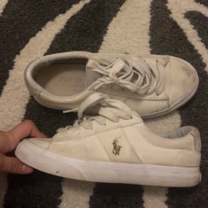 Vita sneakers från Polo Ralph Lauren - Snygga vita sneakers från Polo Ralph Lauren med klassisk låg profil och rund tå. Skorna är inte slitna men har gått med de ute så de är lite smutsiga men eftersom att det är så lite är det enkelt att åtegärda. Men de är trendiga och basic om det är det du söker.