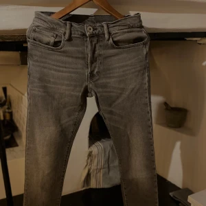 Grå jeans från G-Star RAW - Säljer ett par grå jeans från G-Star RAW Originals med snygg tvättad look och klassiska fem fickor. Jeansen har rak passform och är tillverkade i slitstark denim. Perfekt för dig som gillar streetstyle och vill ha ett par jeans med cool attityd.