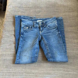 Blå jeans från Gina Tricot - Snygga blå jeans från Gina Tricot med klassisk femficksdesign och dubbla knappar i midjan. Jeansen har raka ben och tydliga slitningar för en cool, avslappnad look. Perfekta till sneakers eller boots.