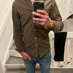 Olivgrön skjorta från Ralph Lauren - Säljer en olivgrön skjorta från Ralph Lauren med orange logga. Säljer då den inte kommit till så mycket användning. Den är skit snygg och perfekt skjorta nu till vintern när de blir lite mörkare ute. 
