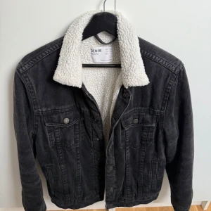 Svart jeansjacka  - Säljer en svart jeansjacka från Bershka med vitt teddyfoder och krage i storlek XS. Jackan har klassiska bröstfickor med knappar och knappstängning framtill. Perfekt för dig som vill ha en cool och varm look under höst och vinter. 