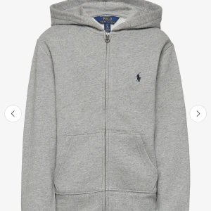 Ralph Lauren - Säljer en klassisk grå hoodie från Polo Ralph Lauren med dragkedja och huva. Tröjan har två fickor framtill och den ikoniska loggan broderad på bröstet. Perfekt för chill dagar och enkel att matcha med jeans eller joggers.