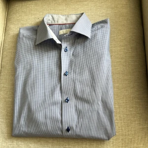 Blårutig skjorta från Eton - Snygg blårutig skjorta från Eton i klassisk modell med blå knappar och röd detaljsöm på insidan av kragen. Skjortan är tillverkad i bomull och har en modern passform. Perfekt för dig som gillar stilrena och tidlösa plagg.