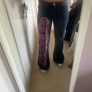 Mörkblå jeans med graffiti-tryck - Unika mörkblå jeans graffiti-inspirerat tryck i lila och rosa längs ena benet där det ”BYBY GIRL”. Lågmidjade. Från Jaded London. Endast använd ett fåtal gånger. Ja brukar ja strl S-M och dessa är precis på gränsen att de passar. Nypris: 1099kr. Tveka inte hör av dig vid eventuella frågor☺️