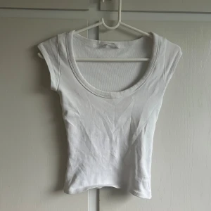 Vit croppad topp från H&M - Enkel och stilren vit croppad topp från zara med rund halsringning och korta ärmar. Perfekt att matcha med jeans eller kjol för en clean look. Gjord i mjuk bomull som känns skön mot huden.