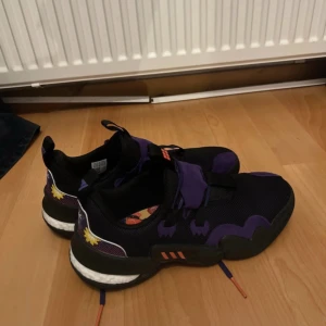 Adidas svarta och lila sneakers strl 46 - Säljer ett par Adidas sneakers i svart och lila med coola detaljer och mönstrad innersula. Skorna har snörning och mesh-ovandel för bra ventilation. Snygga kontrastfärger och unika grafiska inslag på sidan gör dem riktigt speciella. Perfekt för dig som gillar streetstyle.