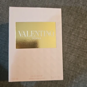 Valentino Donna Eau de Parfum 100ml - Lyxig parfym från Valentino, Donna Eau de Parfum, 100ml. Flaskan är transparent med ett diamantmönster och har en guldig etikett och kork med nitar. Doften är feminin och elegant, perfekt för dig som gillar exklusiva designerparfymer.