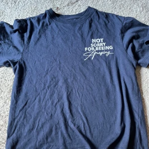 Mörkblå t-shirt med texttryck - Mörkblå t-shirt med vit texttryck både fram och bak. På bröstet står det 'Not sorry for being amazing' och på ryggen 'My time is devoted to positive growth and amazing moments'.