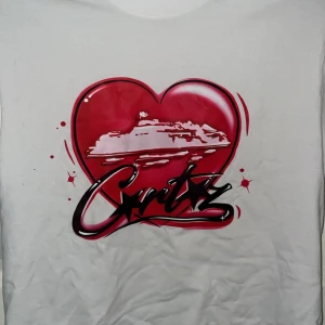 Cortiez T-shirt - Vit t-shirt från Cortiez med ett stort rosa hjärta på bröstet. Snygg graffiti-inspirerad text och stjärndetaljer. Klassisk passform och rund hals. Perfekt för dig som gillar unika prints och streetstyle.