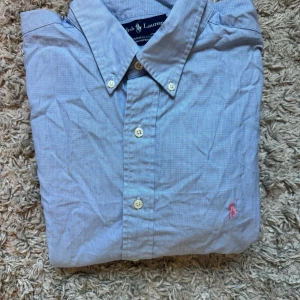 Bulk 2x - Klassisk beige skjorta från Ralph Lauren med button-down krage och broderad logga på bröstet. Skjortan har knappar framtill och är tillverkad i mjuk bomull. Perfekt för en stilren och avslappnad look.