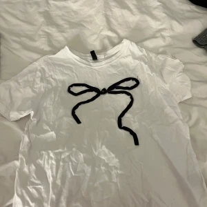 Vit t-shirt med svart rosett från Divided - Hej! Säljer nu min vita t-shirt från H&M i storlek S med en svart rosett framtill (passar också XS). Klassisk rund hals och korta ärmar. Säljer då den inte används, använd 2-3 ggr💞💞