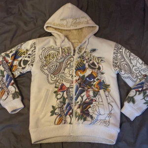 Tattoo-inspirerad hoodie från Really Point - Säljer en vit hoodie från Really Point med sjukt coola tattoo-inspirerade motiv i färg och svartvitt. Tröjan har dragkedja, huva med snörning och mysigt foder. Färgglada detaljer med blå panter, rosor och old school-prints. Lite smutsig på armarna men går bort i tvätten!