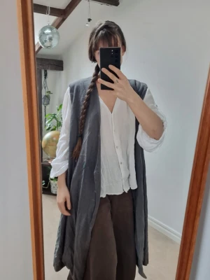 Green long vest - Long green vest with 2 buttons to close it. Soft fabric with 55% linen, 45% viscose. The color on the photos are a bit misleading - it's a foresty green-grey color in reality. I would say that the 4th picture shows the green best. No defects. Length: 100 cm. Probably fits everything from oversized on S to XL 