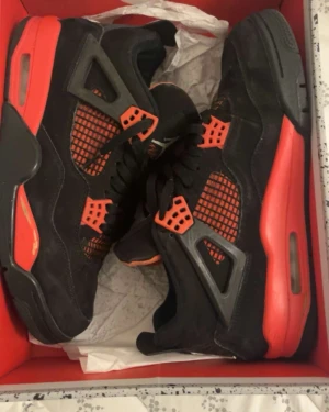 Nike Air Jordan 4 Retro svart/röd - Säljer ett par Nike Air Jordan 4 Retro i svart och rött med klassisk Jumpman-logga på hälen. Skorna har meshpaneler, snörning och en robust sula med synlig Air-enhet. Ovandelen är i mocka och detaljer i plast. Perfekta för dig som gillar streetwear och sneakers med attityd. Passar mindre än 44.