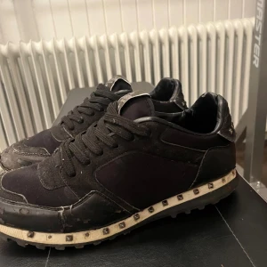 Rockrunners  - Svarta Rockrunner med coola silverfärgade nitar runt sula och häl. Skorna har snörning, platt sula och rund tå. Materialmix av mocka och textil ger en schysst kontrast. Perfekt för dig som gillar edgy designerstil. Skick 6,5/10