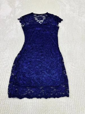 Mörkblå spetsklänning med blommönster - Supersnygg mörkblå kortklänning i spets med blommigt mönster. Klänningen har korta ärmar, rund halsringning och är fodrad med ett glansigt innerfoder. Perfekt för dig som vill sticka ut med en elegant och feminin look.