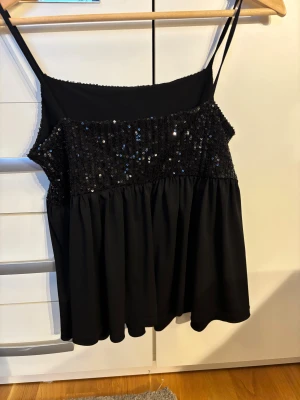 Svart paljettlinne från Gina Tricot - Säljer ett svart linne från Gina Tricot med smala axelband och glittriga paljetter över hela överdelen. Toppen har en loose passform med ett flowy fall nedtill och är perfekt för att sticka ut. Materialet är mjukt och bekvämt, och paljetterna ger en extra touch av glam. Har aldrig använt den och den har bara legat i min garderob, vill att det ska komma till användning💕🫰🏼