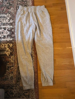 Grå mjukisbyxor från C, storlek M - Säljer ett par grå mjukisbyxor från C i storlek M. Byxorna har resår i midjan och vid bensluten för skön passform. Tillverkade i mjukt bomullsmaterial, perfekta för chill dagar hemma eller när du vill vara bekväm. Klassisk look utan synliga detaljer.