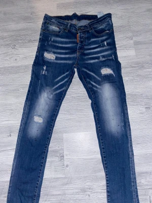 Blå Dsquared2 skinny jeans med slitningar - Snygga blå jeans från Dsquared2 med coola slitningar och distressed detaljer. Modellen är slim och klassisk femficksdesign. Jeansen har tydliga blekta partier och råa kanter vid slitningarna för en trendig look. Perfekta för dig som gillar streetstyle.