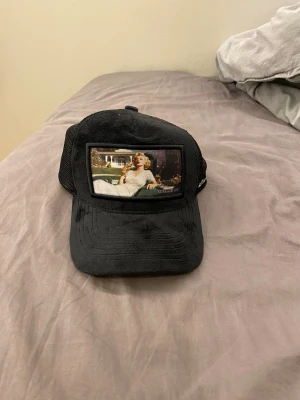 Svart Maggiore meshkeps med motiv - Snygg svart keps från Maggiore med mesh på sidorna och bak, samt ett coolt motiv framtill. Kepsen har justerbar snapback och en metallogo på sidan. Insidan är dekorerad med Maggiore-band. Perfekt för dig som vill sticka ut med en unik accessoar.