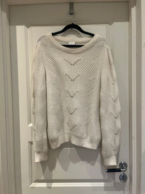 Vit stickad tröja från Vila - Säljer en vit stickad tröja från Vila i storlek M. Tröjan har ett snyggt hålmönster framtill och på ärmarna, rundad hals och ribbade muddar. Perfekt för dig som gillar en chill och stilren look under höst och vinter.