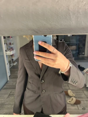 Mörkgrå kavaj från H&M - Snygg mörkgrå kavaj från H&M med klassisk krage och två knappar framtill. Kavajen har figurnära passform, långa ärmar och fickdetaljer. Perfekt för dig som vill ha en stilren och clean look. Materialet är mjukt och känns bekvämt mot kroppen. Det står storlek 38 men den är inte som en 38, den är som en 34!