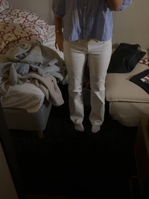 Vita bootcut jeans med normal passform - Säljer ett par vita lågmidjade jeans med bootcut-modell och normal passform. Byxorna har klassisk femficksdesign, dragkedja och knapp framtill. Snygga att styla med både skjorta och t-shirt. Materialet är stadigt och ger en clean look.