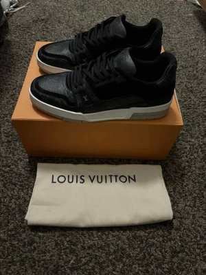 Louis Vuitton svarta sneakers i skinn - Svarta Louis Vuitton sneakers med klassisk monogramdetalj i skinn och syntet. Låg modell med rund tå, snörning och vit platt sula. Snyggt LV-märke på sidan och bak, tillverkade i Italien. Perfekt för dig som gillar exklusiv streetstyle. Dom är i storlek 8,5 som passar dig med s43. Självklart är dom äkta, köpt av Saint garms hemsida som även har en plick konto. Tveka inte med att ställa frågor 