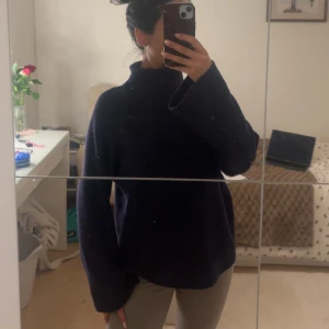 Mörkblå stickad polotröja NA-KD - Mysig mörkblå stickad polotröja från NA-KD med breda, långa ärmar och ribbad hög krage. Tröjan har en loose passform och är perfekt för att hålla sig varm under kyliga dagar. Enkel och stilren design som är lätt att matcha med olika outfits.