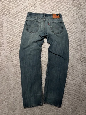 Levi's 505 blå jeans W33 L34 - Säljer ett par klassiska Levi's 505 jeans i blå tvätt med raka ben och normal passform. Jeansen har små slitningar bak men inget som stör. Perfekt för dig som gillar tidlös denimstil.