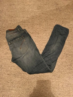 Dondup George jeans blå, storlek 28 - Snygga dondup jeans i klassisk blå tvätt med lätt slitning. Modellen är George, slim fit med fem fickor och detaljerade sömmar på bakfickorna. Perfekt passform för dig som gillar en modern och stilren look. De står 28 på lappen inuti men skulle säga att de passar även mindre