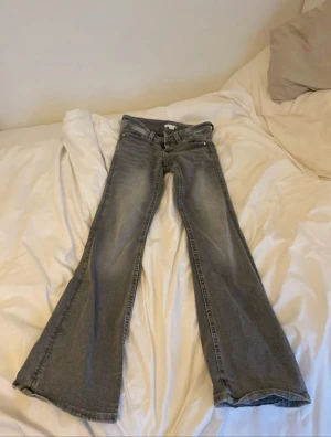 Grå bootcut jeans med flätade fickor - Säljer ett par grå jeans med snygg bootcut passform och coola flätade detaljer på bakfickorna. Jeansen har klassisk femficksdesign, dragkedja och knapp framtill. Materialet är jeans och färgen är en tvättad grå ton som ger en chill vibe.