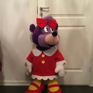 Ingen väst på bilden - Bilden visar ett stort gosedjur utklätt i röd klänning och röd rosett, men ingen väst syns. Bingo Lotta stor 