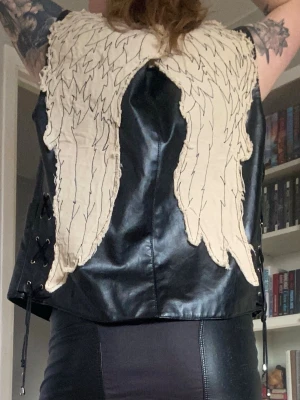Daryl Dixon-väst - Denhär pärlan var fyndad på Tradera för några år sen, men har använts väldigt sparsamt. Svart läderväst i (förmodligen fejk) skinn/läder med snörning längst sidorna och broderade vingar på ryggen. De verkar ha varit ditlimmade, så ingen garanti på hur väl de sitter, men lite textillim till skadar nog inte. Storlek XL i ”mansmodell” är min gissning, så väldigt rymlig. Perfekt för cosplay, halloween, eller en vanlig prommis till lokala mataffären. Läs gärna bion innan köp!