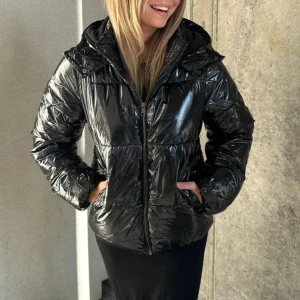 Svart glansig pufferjacka med huva - Säljer nu en svart glansig pufferjacka från Nelly som jag använt ett fåtal gånger. Jackan är slutsåld och kommer förmodligen inte in igen. Jackan är i strl XXS och har inga synliga defekter🩶Köptes för 459kr och säljs nu för 150!