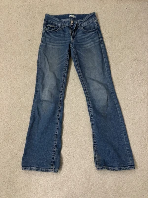 Blå bootcut jeans från Gina Tricot - Snygga blå jeans från Gina Tricot i storlek 164. Modellen har bootcut-ben, klassisk femficksdesign och låg midja. Jeansen är tillverkade i jeansmaterial med lätt slitning framtill för en cool look.
