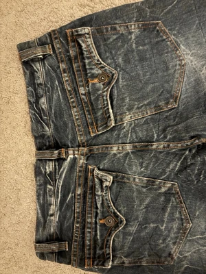 Mörkblå bootcut jeans  - Säljer ett par mörkblå jeans från Nolita med coolt slitna detaljer och kontrastsömmar. Materialet är klassisk denim och passformen är bootcut! 💘