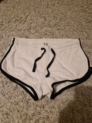 Vita sportiga shorts från FASISTER - Säljer ett par vita sportiga shorts från new yorkeri storlek S. De har svarta kanter och snörning i midjan för en snygg kontrast. Perfekta för träning eller chill dagar. Mjukt material och klassisk retrostil.