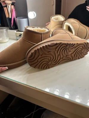 Beige boots med foder från Nelly - Mysiga beige boots från Nelly med fluffigt vitt foder på insidan. Skorna har rund tå, platt sula och är tillverkade i mockaimitation. Perfekta för kalla dagar och har en enkel, stilren design.