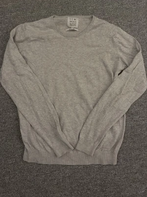 Ljusgrå tröja från S.C.W. Slim fit - En stilren ljusgrå tröja från S.C.W. i slim fit-modell. Tröjan har rund halsringning, långa ärmar och ribbade muddar vid ärmslut och nederkant. Perfekt för dig som gillar enkel och clean stil.