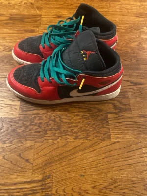 Nike Air Jordan 1 svart/röd sneakers - Säljer ett par Nike Air Jordan 1 sneakers i svart och rött med vita detaljer och gröna skosnören. Skorna har klassisk hög siluett, rund tå och platt sula. Överdelen är i skinn och textil, med ikonisk Jumpman-logga på plösen och vinge på sidan. Och har änvönt dom två gånger. Finns i Stockholm. Ingen låda