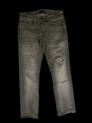 Grå jeans från Jack & Jones - Ett par basic slimfit jacknjones jeans som inte kommer till användning. Stl: 28/32 men omsydd till 30 på längden. Skick 8/10 pga litet hål vid skrevet men går att fixas annars inga andra skavanker. Det går även att ge bud!