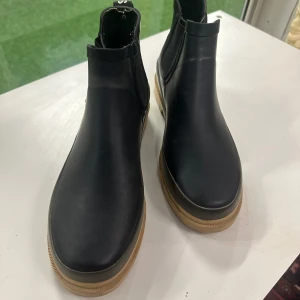 Svarta stilren gummistövlar från Angulus38 - Snygga svarta gummistövlar från Angulus med grov beige sula och elastiska paneler på sidorna. Stövlarna är utmärkt skick och har dragflik baktill med Angulus-logga. Perfekta för dig som vill ha en stilren gummistövlar 