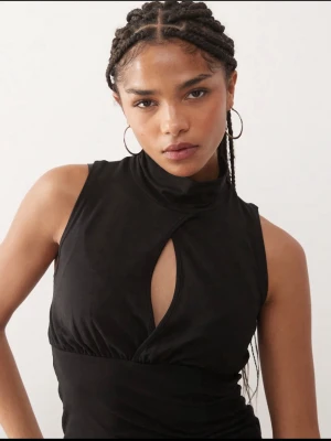 Svart ärmlös polotopp med cut out - Säljer en svart ärmlös polotopp med cool cut out-detalj framtill. Toppen har hög hals och figurnära passform som framhäver siluetten. Toppen är väldigt snygg på och är väldigt bekväm. Skriv om ni vill ha fler bilder.