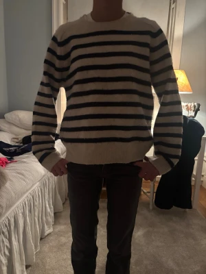 Randig stickad tröja i vitt och svart - Säljer en mysig stickad tröja med breda svarta och vita ränder. Tröjan har en relaxed passform, rund halsringning och långa ärmar med ribbade muddar. Perfekt för kyliga dagar och enkel att styla med jeans eller kjol.