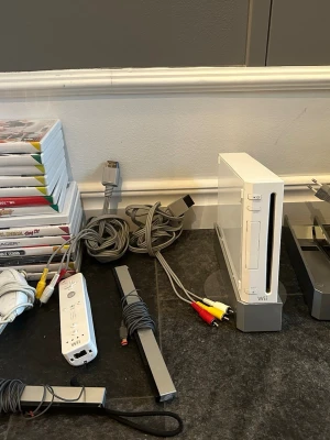 Nintendo Wii - Nintendo Wii spelkonsol i vitt, komplett med originalkablar, sensorbar och minst en Wii Remote. Konsolen är i gott skick och fungerar, vilket syns på den blå lysdioden. Perfekt för familjespel och partyspel. Några mindre bruksspår kan förekomma.några spel funkar inte 