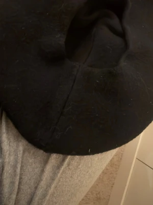 Svart basker med pärldetaljer - Säljer en svart basker med vita pärlor i cirkelformade mönster. Baskern har en klassisk rund form och är tillverkad i ull, vilket gör den både varm och stilren. Perfekt accessoar för att lyfta din outfit med en unik touch.