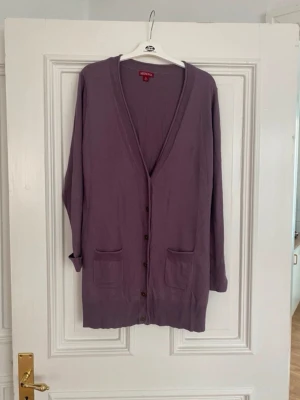 Lila kofta från Merona, XL - Lång, lila kofta från Merona i storlek XL. Koftan har v-ringning, knappar framtill och två fickor. Tillverkad i mjukt material som känns skönt mot huden. Perfekt för lager på lager och chill dagar.