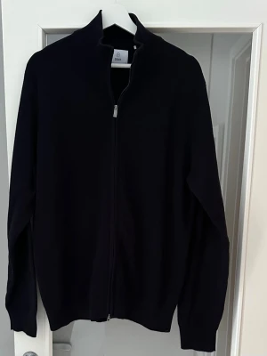 Marinblå zip cardigan Roman från Bläck, herr stl L - Stilren mörkblå zip-kofta från Bläck med hel dragkedja framtill och hög krage. Herr stl L. Använd ett fåtal gånger, ser ut som ny. 